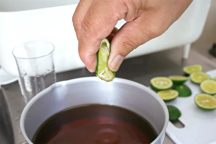 すだちを手で絞って、めんつゆに入れる様子
